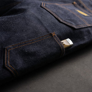 Close-up of dark blue denim fabric with a tool in a side pocket on a gray background
