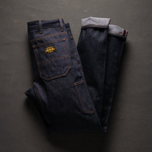 Folded dark blue jeans with a yellow flower patch on a gray background
